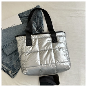 Flat lay of a silver quilted tote bag with black straps alongside lifestyle accessories
