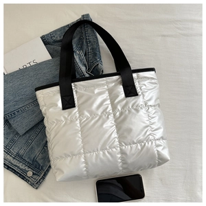 Close-up of quilted silver puffer tote bag with black straps on a textured background
