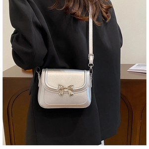 Detail of silver crossbody bag featuring golden metal bow clasp and adjustable strap