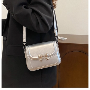 Silver metallic square crossbody bag with a gold bow accent worn by a model
