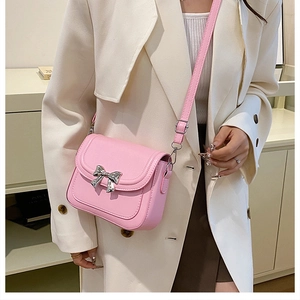 Close-up of pink crossbody bag with silver bow ornament worn on a white blazer