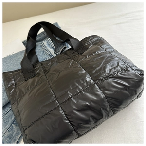 Detail of black quilted tote bag with large square stitching and wide webbing handle