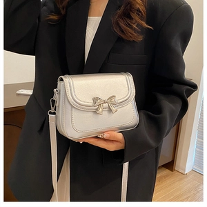 Silver bow shoulder bag shown on a model with metallic finish and minimalist design