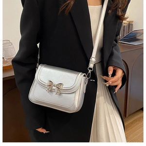 Silver metallic crossbody bag with a bow buckle shown worn by a model in a home setting