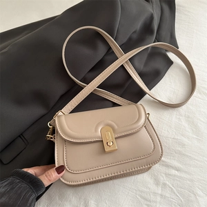 Modern beige crossbody square bag with golden swivel lock on soft fabric background