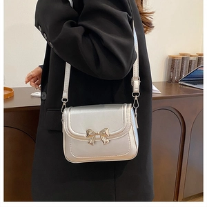 Détail du sac bandoulière argenté avec boucle nœud dorée sur un blazer noir