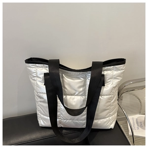 Close-up of silver quilted tote bag featuring black woven handles and puffer fabric detail