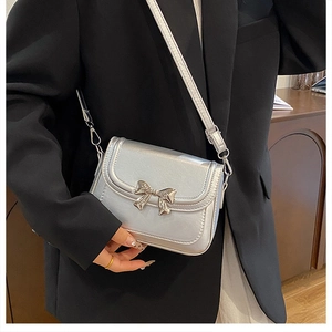 Detail of silver metallic crossbody bag featuring an elegant bow metal buckle and flap