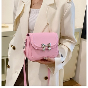 Detail of pink small crossbody bag with silver metal bow and matte finish on shoulder strap
