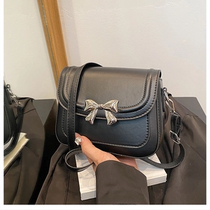 Detail of black crossbody square bag featuring a silver metal bow clasp and leather texture