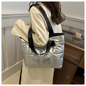 Silver quilted tote bag with metallic finish shown on model in a modern indoor setting