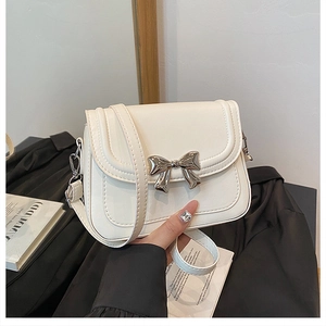 Detailed view of white crossbody bag with a polished silver metal bow and thin strap