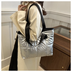 Modern silver quilted puffer tote bag with black straps worn by a model in a room