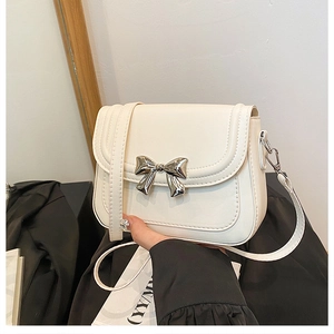 Détail d'un sac bandoulière beige avec boucle nœud en métal argenté poli et coutures fines