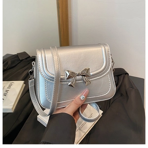 Close-up of a silver crossbody bag with a metallic bow buckle and shiny finish
