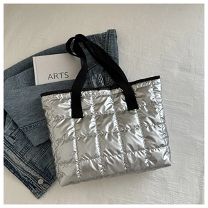 Top-down view of a silver quilted puffer tote bag with broad black strap and artsy props