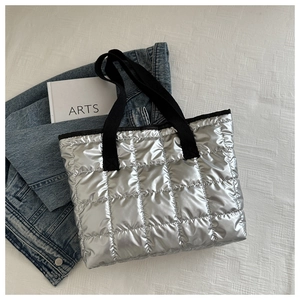 Detail of silver metallic quilted tote bag with black canvas straps on textured fabric