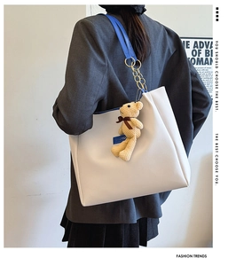 Detail of white leather tote with blue straps, gold chain and plush bear charm accessory