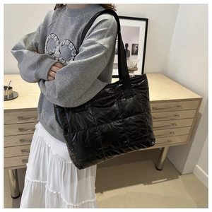 Detail of a black quilted tote bag in glossy nylon fabric with thick padded texture