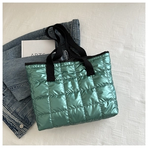 Flat lay of a green quilted tote bag with black woven handles and a minimalist book
