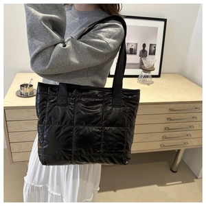 Detail view of a black quilted tote bag worn with a casual outfit in a cozy home setting