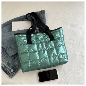 Flat lay of metallic green quilted handbag with black handles next to a denim jacket