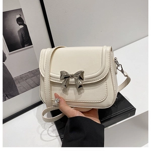 Detail of a cream faux leather crossbody bag featuring a silver metal bow decoration