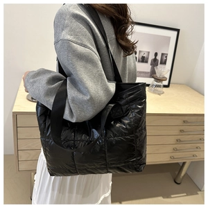 Detail of a large black quilted tote bag with shiny finish worn as a shoulder bag