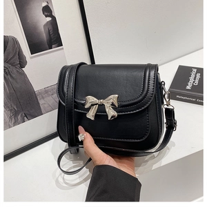 Close-up of black crossbody square bag with metallic silver bow detail and leather strap