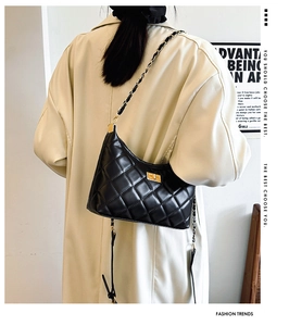 Close-up of black quilted shoulder bag with gold chain strap worn over a beige trench coat