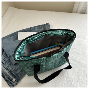 Detail view of emerald green quilted tote bag with square embossing and black handles