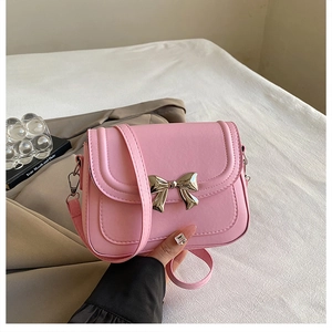Detail view of pink crossbody bag with a gold metal bow and magnetic flap closure