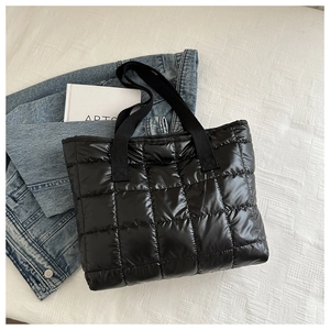 Close-up of black quilted puffer tote bag with glossy nylon texture and wide straps