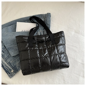 Detail of black quilted tote bag with padded texture and webbing handles on denim fabric