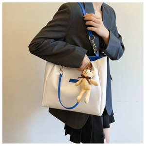 White tote bag with blue straps and brown bear charm worn over a grey blazer suit