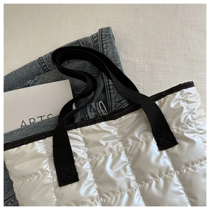 Close-up of white quilted tote bag with black canvas handles and glossy finish