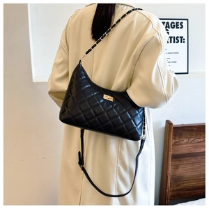 Detail of black quilted shoulder bag featuring gold twist lock and chain strap on a model