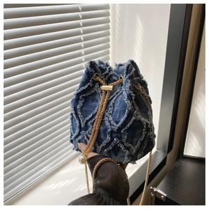 Detail of denim bucket bag showing diamond quilted fringe and golden chain strap with pearl