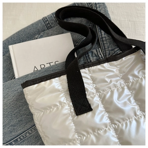 Detail of white quilted tote bag with black strap on denim jacket and artsy book