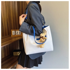 Minimalist white tote bag with blue straps and cute bear charm shown on a shoulder
