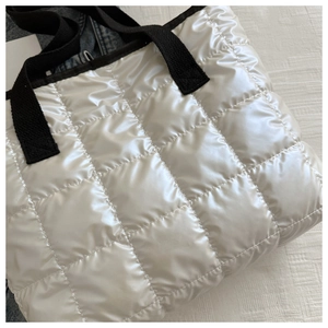 Close-up of pearl white quilted handbag with glossy finish and black woven strap handles