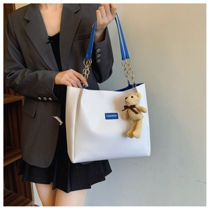 Close-up of white leather tote bag featuring bright blue straps and a gold chain handle