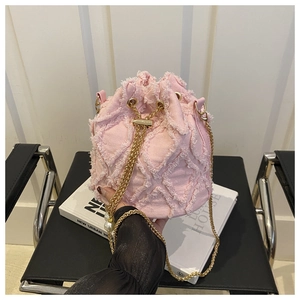 Détail du sac seau en denim rose avec motifs matelassés effilochés et chaîne perle