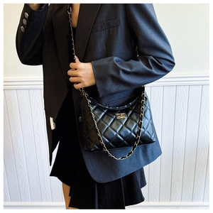 Detail of the black quilted leather texture and gold metal clasp on a chain tote bag