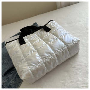 Detail of white quilted tote bag featuring plush texture and black contrast handles