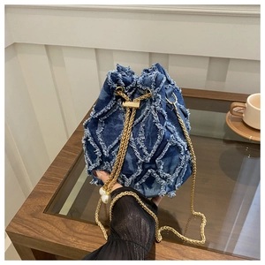 Dettaglio borsa a secchiello in denim blu con frange trapuntate e tracolla di perle