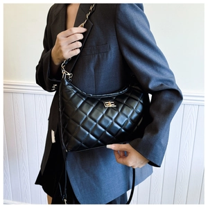 Detail of black quilted shoulder bag featuring gold twist lock and chain strap on model