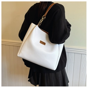 Detailed view of white tote bag with brown leather label and golden chain strap