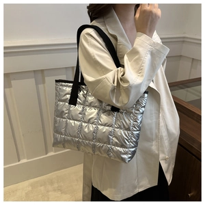 Detail of silver quilted puffer bag with glossy metallic finish and black woven strap