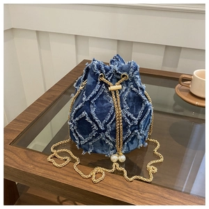 Détail du sac seau en denim bleu avec texture effilochée et détails de perles au cordon